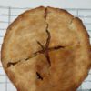 A fresh baked apple pie resting out of the over on a cooling rack