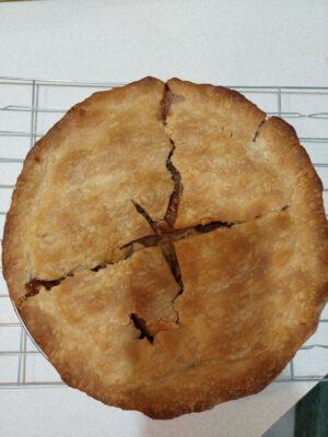 A fresh baked apple pie resting out of the over on a cooling rack